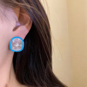 Detailed view of silver-plated hollow mesh stud earrings with blue beaded border on ear