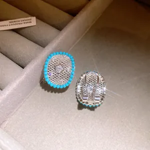 Close-up detail of silver-tone hollow grid earrings with turquoise beads and central zircon.
