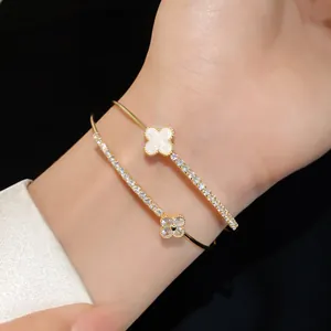 Detail of a gold-tone double-layer bracelet with sparkling zircons and a white clover motif.