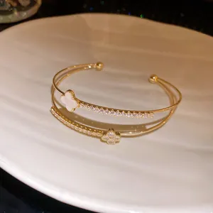 Elegant double-layer gold bangle with pavé zircon flower charms on white shell plate.