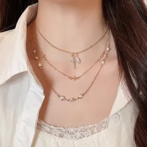 Elegante collana dorata a più strati con perle e ciondolo a croce di strass su modella
