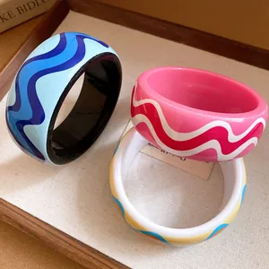 Vue détaillée de trois joncs en résine colorés avec des motifs ondulés sur un plateau.