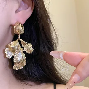 Detailed macro view of vintage gold metallic leaf drop earrings worn on a model's ear