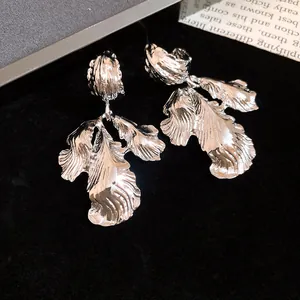 Detailed macro shot of silver leaf-shaped metallic earrings on textured dark background