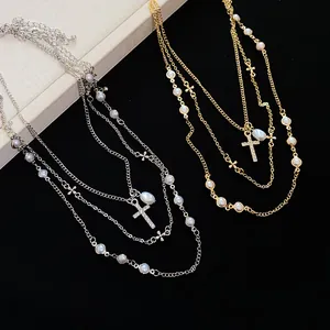 Dettaglio di collana multistrato con perle bianche e ciondoli a croce con strass