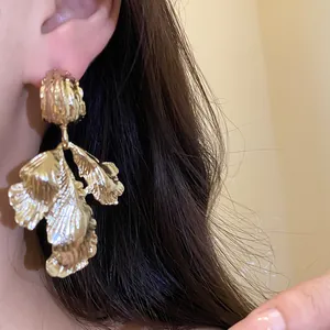 Close-up detail showing the metallic texture of vintage gold leaf pendant earrings on an ear.