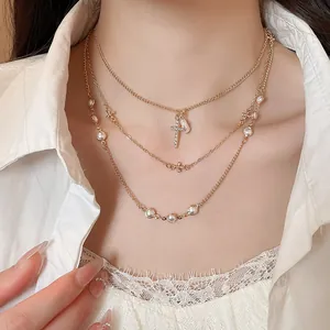 Collana a strati dorata con perle eleganti e ciondolo a croce scintillante in primo piano.