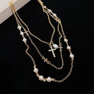 Vista dettagliata di una collana d'oro a tre strati con perle eleganti e croce di strass lucenti.