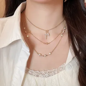 Dettaglio di una collana a più strati dorata con perle e ciondolo a croce di diamanti
