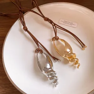 Dettaglio di pendenti a forma di conchiglia oro e argento con cordini marroni regolabili.