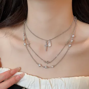 Dettaglio di una collana d'argento a più strati con perle e croce con strass luccicanti.