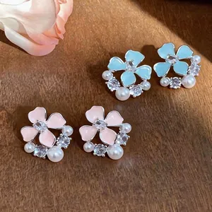 Elegant enamel flower stud earrings with zircon and pearls shown on a wooden background