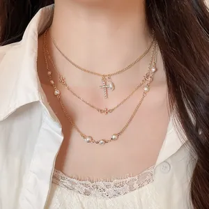 Primo piano di una collana a più strati dorata con croce di strass e ciondoli di perle