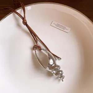 Primo piano di un ciondolo a forma di conchiglia d'argento su una collana di cordoncino marrone