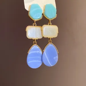 Close-up of retro palace style resin earrings with green, cream, and blue stone pendants.