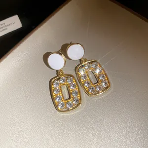 Detailed view of elegant gold drop earrings featuring sparkling rhinestones and white studs
