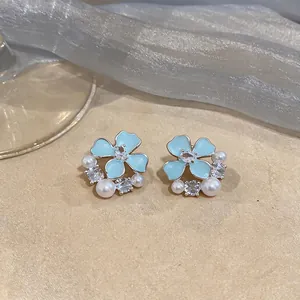Detailed close-up of light blue enamel flower stud earrings with pearls and zircons