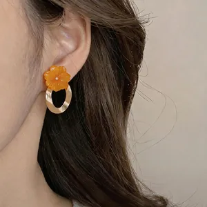 Elegant orange resin flower earrings with gold oval rings on a model ear.