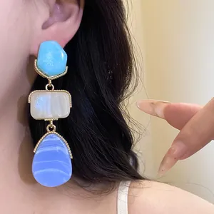 Detail shot of multi-colored resin drop earrings with gold framing on an Asian model