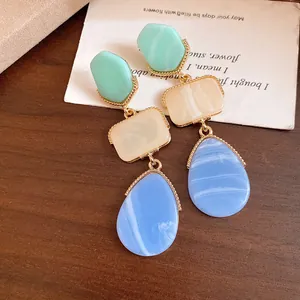 Close-up view of vintage resin drop earrings with blue teardrop and green hexagon stones.
