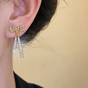 Close-up of 14k gold plated bow earrings with sparkling dangling zircons on ear