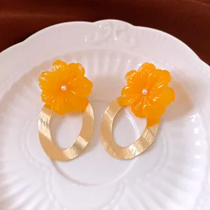 Vibrant orange resin flower earrings with large gold oval hoops on a white plate