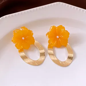 Close-up view of elegant orange resin flower earrings with textured gold oval metal hoops.