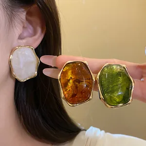 Detalle de pendientes ovalados de resina irregular vintage en tonos blanco, ámbar y verde