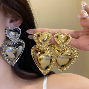 Close-up view of chunky vintage metallic heart drop earrings in gold and silver finish