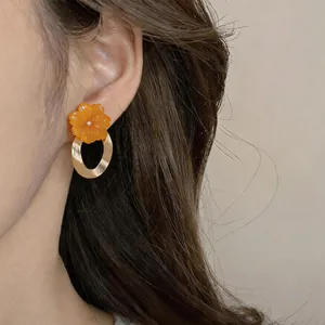 Close-up view of orange resin flower earrings with gold metal rings and silver needles.