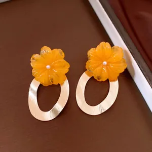 Close-up of orange resin flower earrings with gold oval hoops and pearl centers.