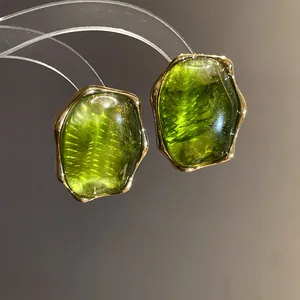 Detalle macro de elegantes pendientes vintage de resina verde con marcos dorados irregulares.