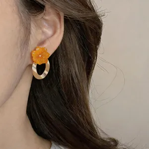Close-up view of elegant orange resin flower hoop earrings worn on the model's ear