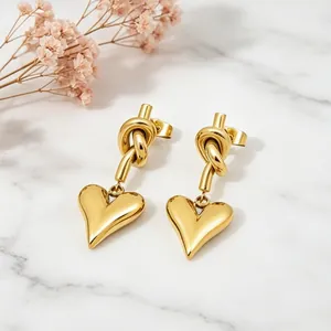 Elegant gold stainless steel knotted heart dangle earrings displayed on white marble