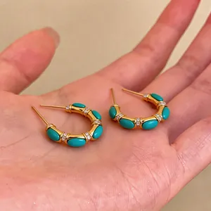 Detail of 18k gold plated C-shaped hoop earrings with turquoise and zirconia stones.