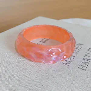 Detail view of stylish orange resin bangle with irregular textured surface and iridescent glow
