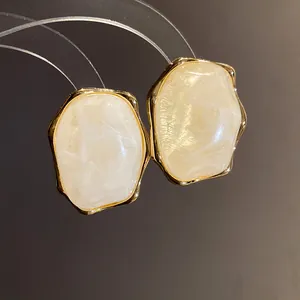 Primer plano de elegantes pendientes ovalados de resina con marcos dorados texturizados