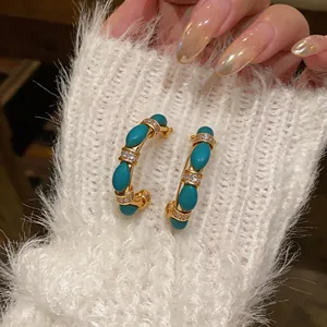 Detail view of 18k gold plated C-shaped earrings with turquoise stones and zircons