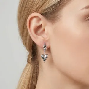 Elegant silver stainless steel knot earrings with puffy heart pendant shown on model's ear