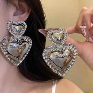 Close-up of oversized retro silver heart dangle earrings showing glossy metallic finish