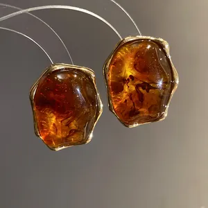 Primer plano de pendientes vintage de resina ámbar con bordes metálicos dorados irregulares