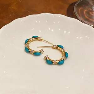 Detailed view of vintage C-shape earrings with turquoise stones and clear zircons.