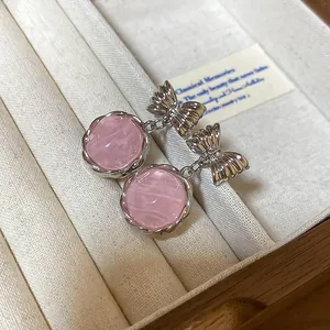 Detailed macro shot of pink round drop earrings with silver bow studs in jewelry box