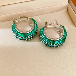 Detailed macro view of silver-tone hoop earrings featuring emerald green baguette crystals