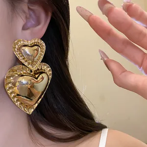 Chunky vintage gold heart dangle earrings with textured edges shown on a model's ear