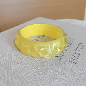 Macro detail of a yellow resin bangle with an irregular bumpy texture on a book.