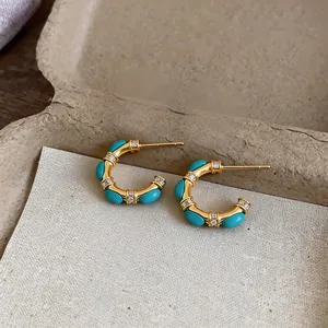 Detailed view of gold C-shaped earrings with turquoise cabochons and zircon accents