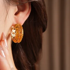Detail view of gold-plated geometric hoop earrings set with orange crystals on ear