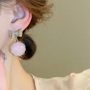 Close-up of pink round drop earring with silver bow knot on ear