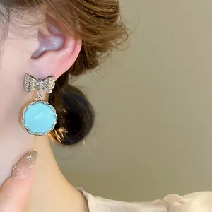 Close-up detail of a silver bow and light blue round pendant earring on a model's ear